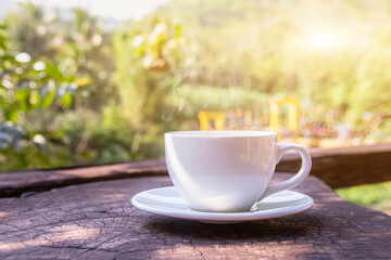 A white cup of hot espresso coffee mugs placed on a wooden floor with morning fog and moutains with sunlight background,coffee morning