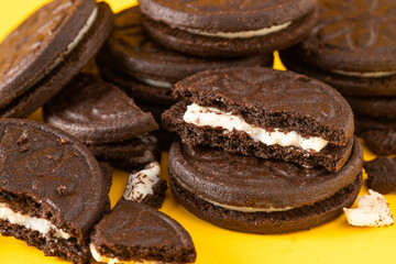 Broken Chocolate sandwich cookies with vanilla cream filling  and  cookies crumbs on yellow background.