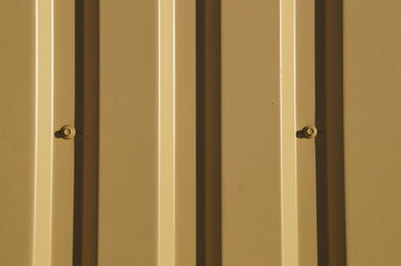 a fragment of a mustard-beige corrugated iron fence with bolts