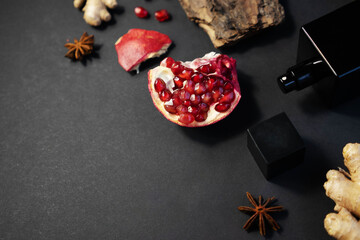 a black perfume bottle with fragments of tree bark, ginger and pomegranate on a dark background. Copy space