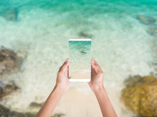 Hand woman Taking sea photo with mobileHand woman holding mobile with sand beach view on blur image of sand beach with white sea soft wave on top view . 