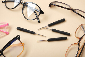 eye glasses and small screwdrivers on beige background, broken glasses, glasses repair concept