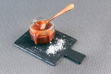 Fototapeta premium Salted caramel in a jar on a gray background on a stone stand. Side view.