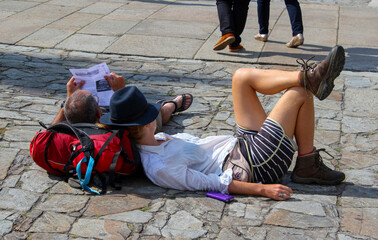 Dos peregrinos descansan acostados sobre sus mochilas en el suelo de la plaza de la catedral de...