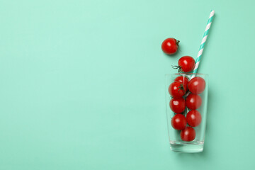 Glass with tomatoes and straw on mint background