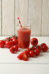Glass with tomato juice and straw and tomatoes on wooden background