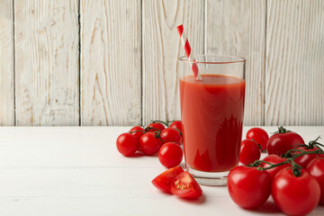 Glass with tomato juice and straw and tomatoes on wooden background