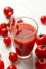 Glass with tomato juice and straw and tomatoes on wooden background
