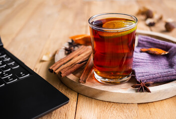 English tea, black tea in glass with spices and laptop on wood backgroung. drink for autumn 
or winter season.
