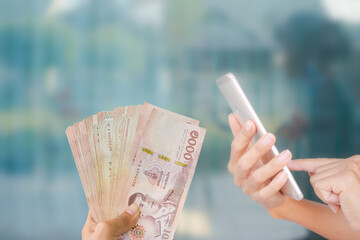 Close up using mobile with thai banknotes 1000 baht on blue background. for accompanying articles...