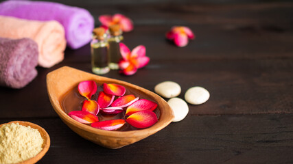 Aromatherapy spa set concept. red plumeria petals floating in clay pot  with thanaka powder and towel, massage oil on wooden background.