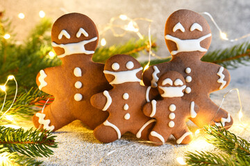 Gingerbread family in a mask. Christmas background. Gingerbread, spruce and lights. Quarantine.