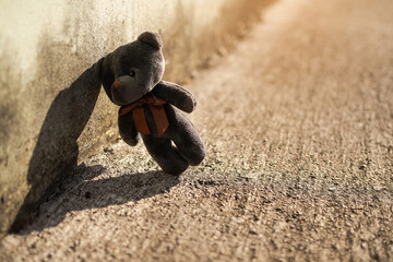 dark silhouette image of alone teddy bear standing on dirty wall. Broken heart or Loneliness...