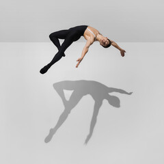 Fototapeta premium Flexible. Stylish young male athlete on white studio background with shadows in jump, air flying. Sportive fit model in motion and action. Body building, healthy lifestyle, style concept.
