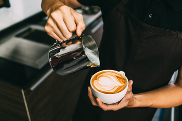 Crop image of a young male barista pouring hot milk into hot espresso black coffee for making Latte...