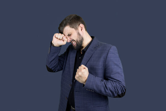 a man with a beard and a blue suit presses his fist to his head showing emotions of pain