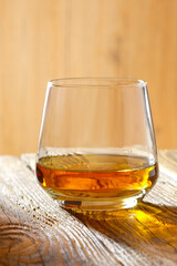 Sniffer glass with whiskey on wooden table in sunlight