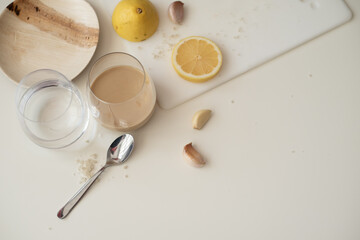 Tahini, lemon and garlic on the white table. How to cook tahini. First step for cooking. Glass of water and tahini. Tahini different from hummus. Traditional food. step 1