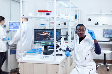 African biochemistry looking at sample on glass slide sitting at her workplace. Black healthcare scientist in biochemistry laboratory wearing sterile equipment.
