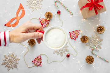 Woman hand with a cup of cappuccino against christmas decorations background.