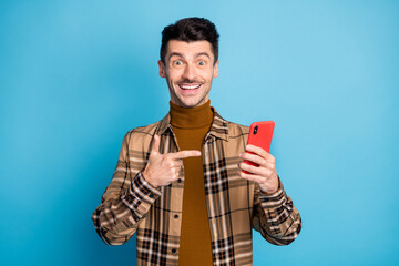 Photo of young happy excited cheerful smiling good mood man pointing finger at phone isolated on blue color background
