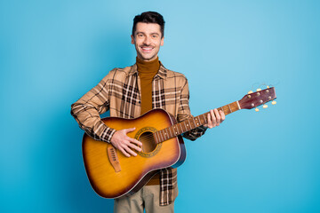 Photo of young happy positive cheerful smiling good mood man playing acoustic guitar isolated on blue color background