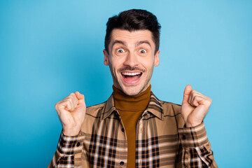 Naklejka premium Portrait of young happy excited cheerful positive shocked man hold fists in victory isolated on blue color background