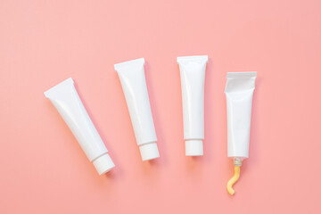 White cosmetic tubes on a pink background. Concept of face and body skin care, cosmetics. Top view, minimalism, flat lay, copy space.