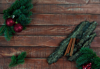 Spruce branches with red Christmas decorations lie on a brown wooden board with a piece of bark and cinnamon stick