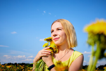Pretty woman on a field with green grass and yellow dandelion flowers in a sunny day. Girl on nature with yellow flowers and blue sky.