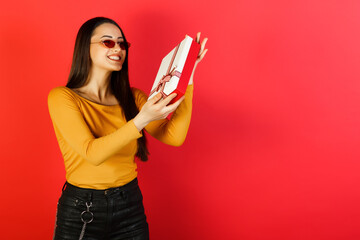 Portrait of happy woman holding present box isolated over red background. Holidays concept.
