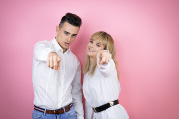 Young couple of girlfriend and boyfriend over isolated pink background pointing with finger surprised ahead, open mouth amazed expression, something on the front
