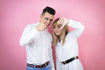 Young couple of girlfriend and boyfriend over isolated pink background Doing thumbs up and down, disagreement and agreement expression. Crazy conflict