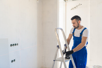 A foreman in overalls marks the wall using a laser level