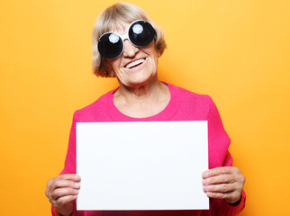 Elderly woman with blank advertising board or copy space. Portrait of handsome expressive grandmother over yellow background.