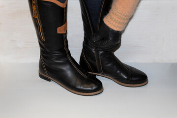 Legs shod in black winter boots. A leather-gloved hand fastens the zipper on the second boot.
