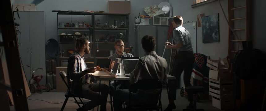 WIDE Group of young people discussing something, brainstorming. Launching their small IT business startup company from garage. Shot with 2x anamorphic lens
