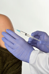 Close-up shot of medical assistant giving an intramuscular injection of a vaccine to arm of young woman in a clinic focus on syringe needle