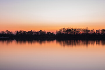 Obraz premium Landschaft und Sonnenuntergang mit Ufer des Sarchinger Weiher mit Spiegelung des Himmels in dem glatten See mit wunderschönen Farben Farbenspiel ohne Wolken, Deutschland