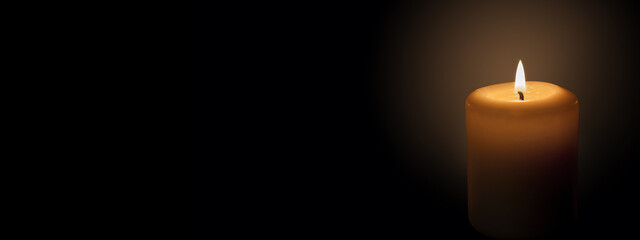 White candle on a black background. The candle flame illuminates the space around it. Banner with space for text.
