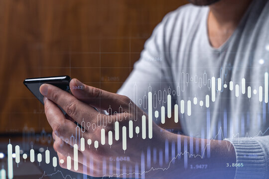 Trader holding in the hands a smart phone and researching stock market to proceed right investment solutions. Internet trading and wealth management concept. Hologram Forex chart over close up shot.