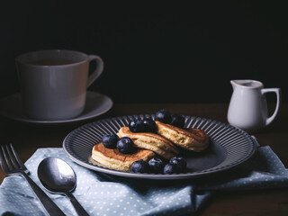 blueberry pancakes in a plate. Traditional food for breakfast or brunch. Homemade fluffy pancakes, cup of coffee, spoon and fork on table. Tasty pancakes with fruit and maple syrup. Food photography