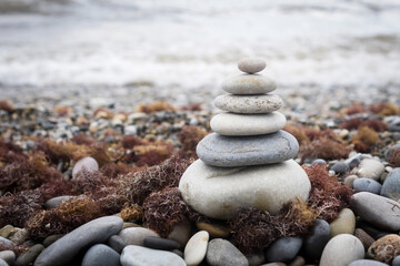 Fototapeta na wymiar pyramid of stones on the beach against the background of sea waves, stone beach and seaweed