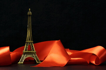 A statuette of the Eiffel Tower surrounded by a red ribbon on a black . The concept of romance, love, travel.