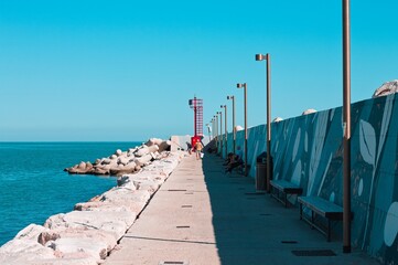 Obraz premium View of the Mediterranean sea from the jetty in the harbour of Pesaro with a red lighthouse (Pesaro, Italy, Europe)
