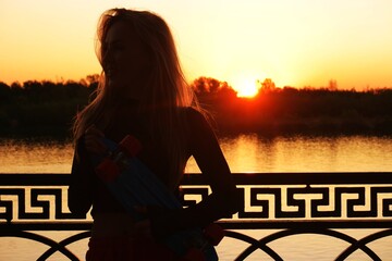 Long haired lady holding skateboard in her hands in front of sunset