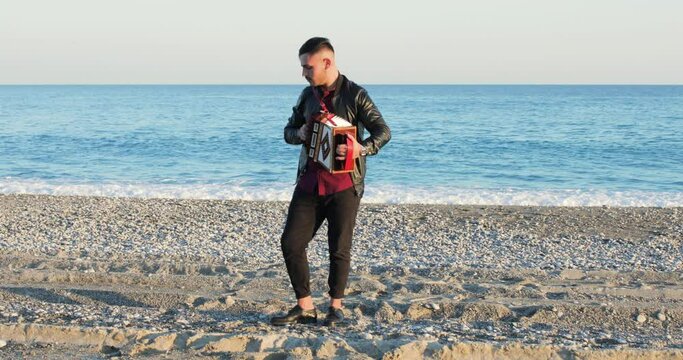 Suonare l'organetto per musica sulla spiaggia in riva al mare da un giovane ragazzo con giacca nera