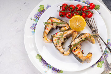 Grilled sturgeon steaks on a white plate with spices, cherry tomatoes and lemon. On a gray...