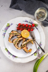 Grilled sturgeon steaks on a white plate with spices, cherry tomatoes and lemon. On a gray background.
