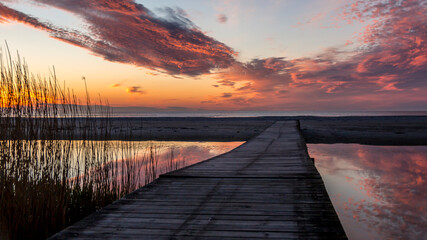 Naklejka na ściany i meble Beautiful sunset. golden, orange, blue colors over the sea. sky full of many colors. bridge over a small lake where the sky is reflected in